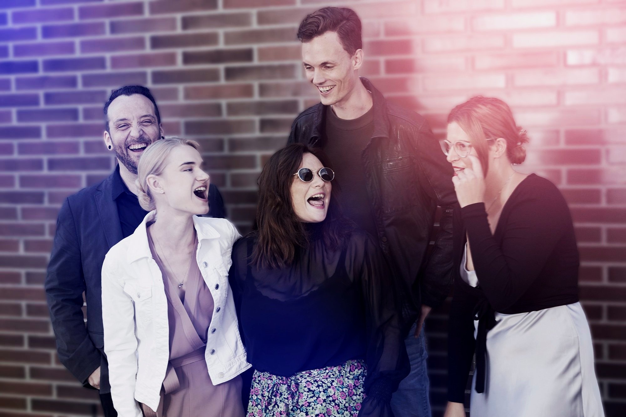Group of five people laughing and talking outdoors against a brick wall.