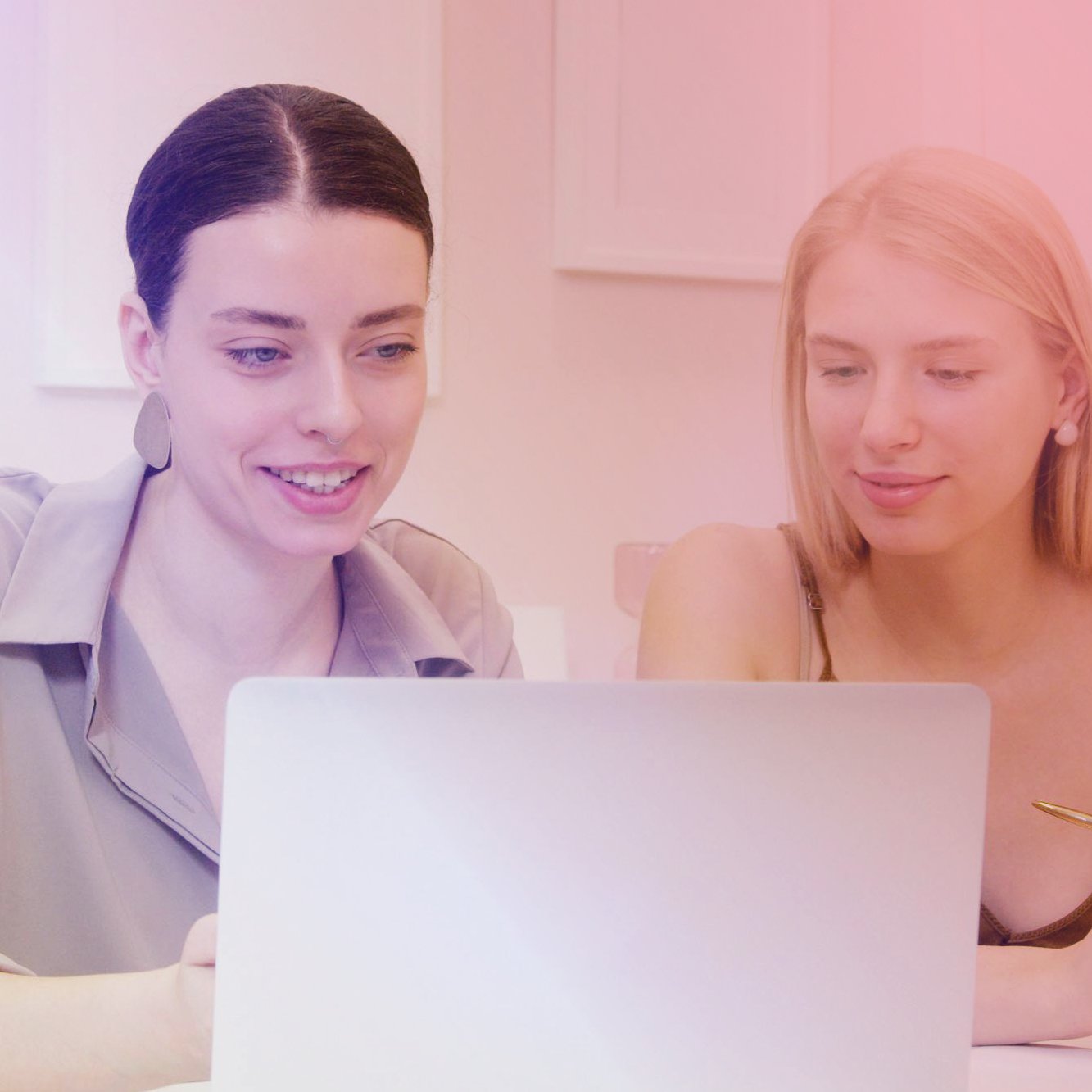 Two women sitting together and looking at a laptop on a table, smiling.