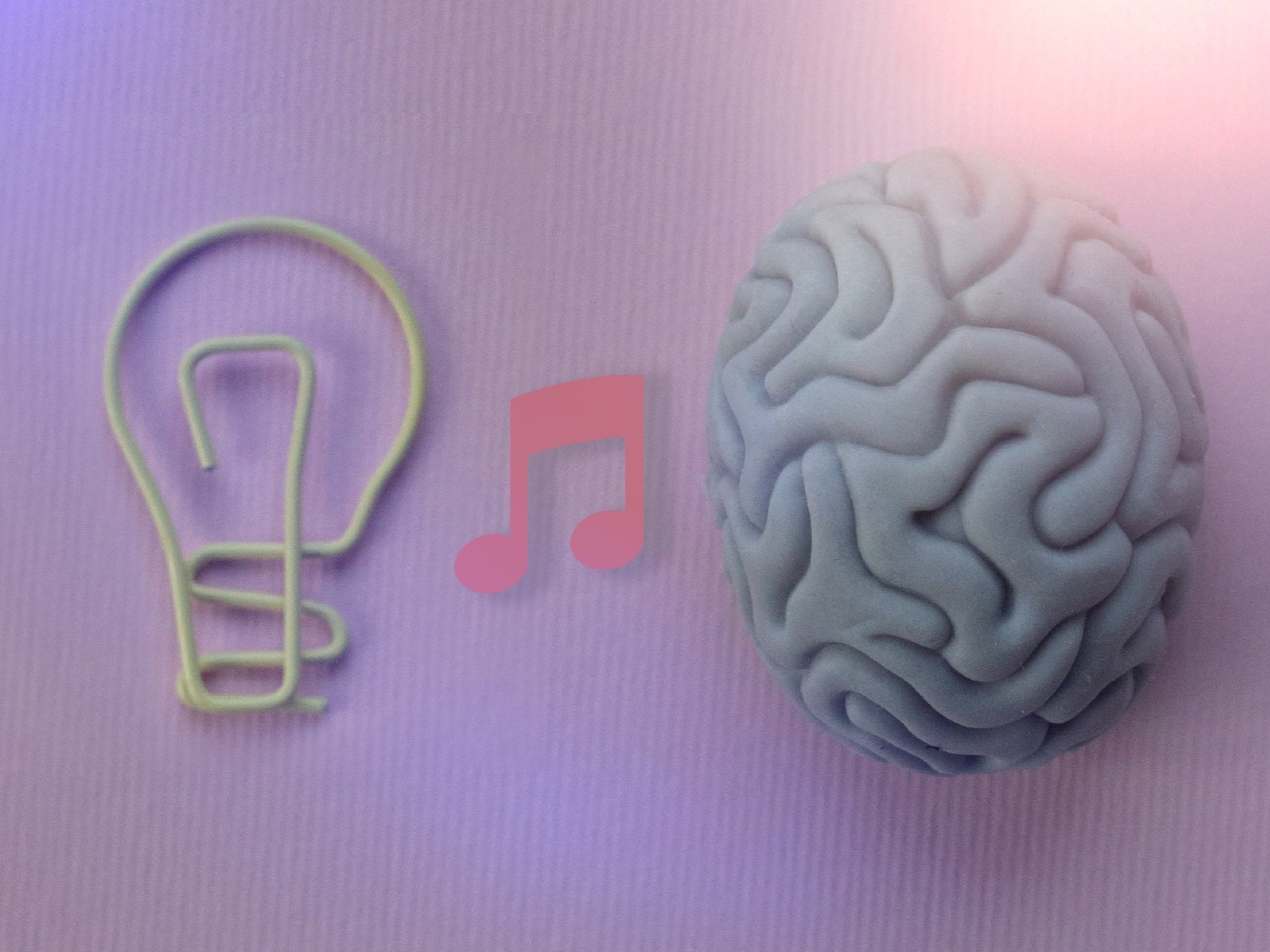 A yellow light bulb-shaped paperclip, a pink music note icon, and a gray brain-shaped object on a pink textured background.