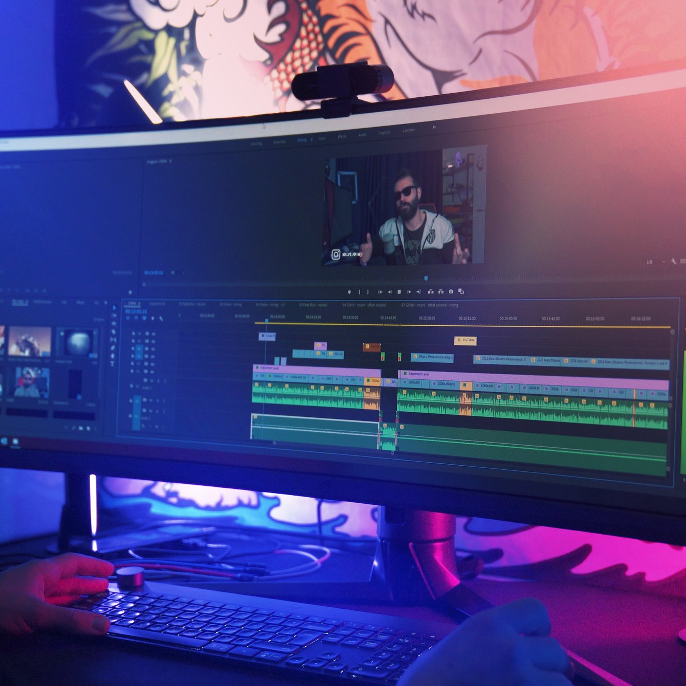 A person editing a video on a computer monitor displaying editing software, with a colorful digital artwork in the background.