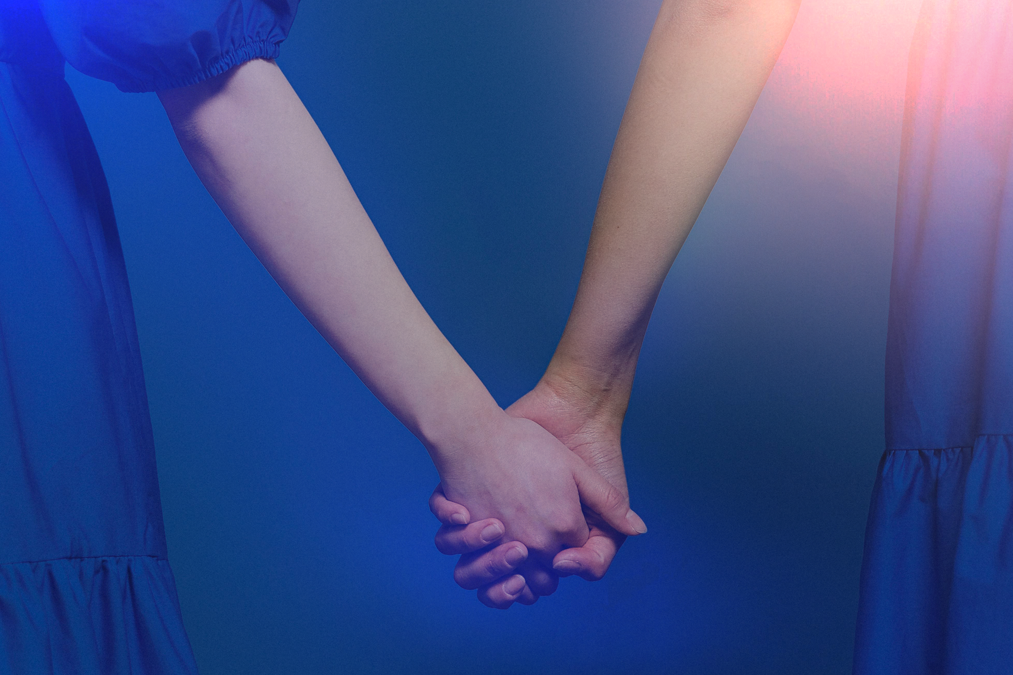 Two people holding hands, one wearing a blue dress with long sleeves, against a blue background with light flares.