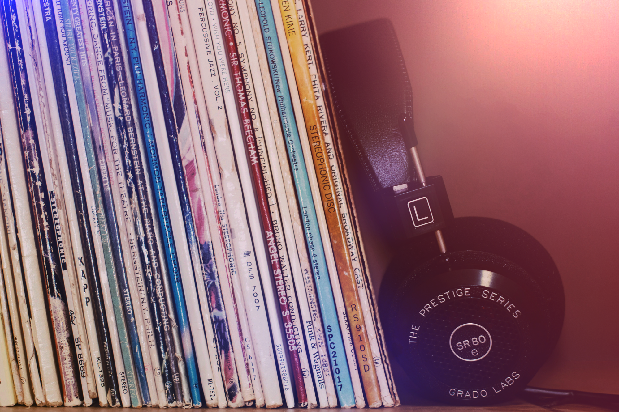 Stack of colorful vinyl records and a black headphone with the brand label 'Grado Labs' and model 'SR80e' resting against them.