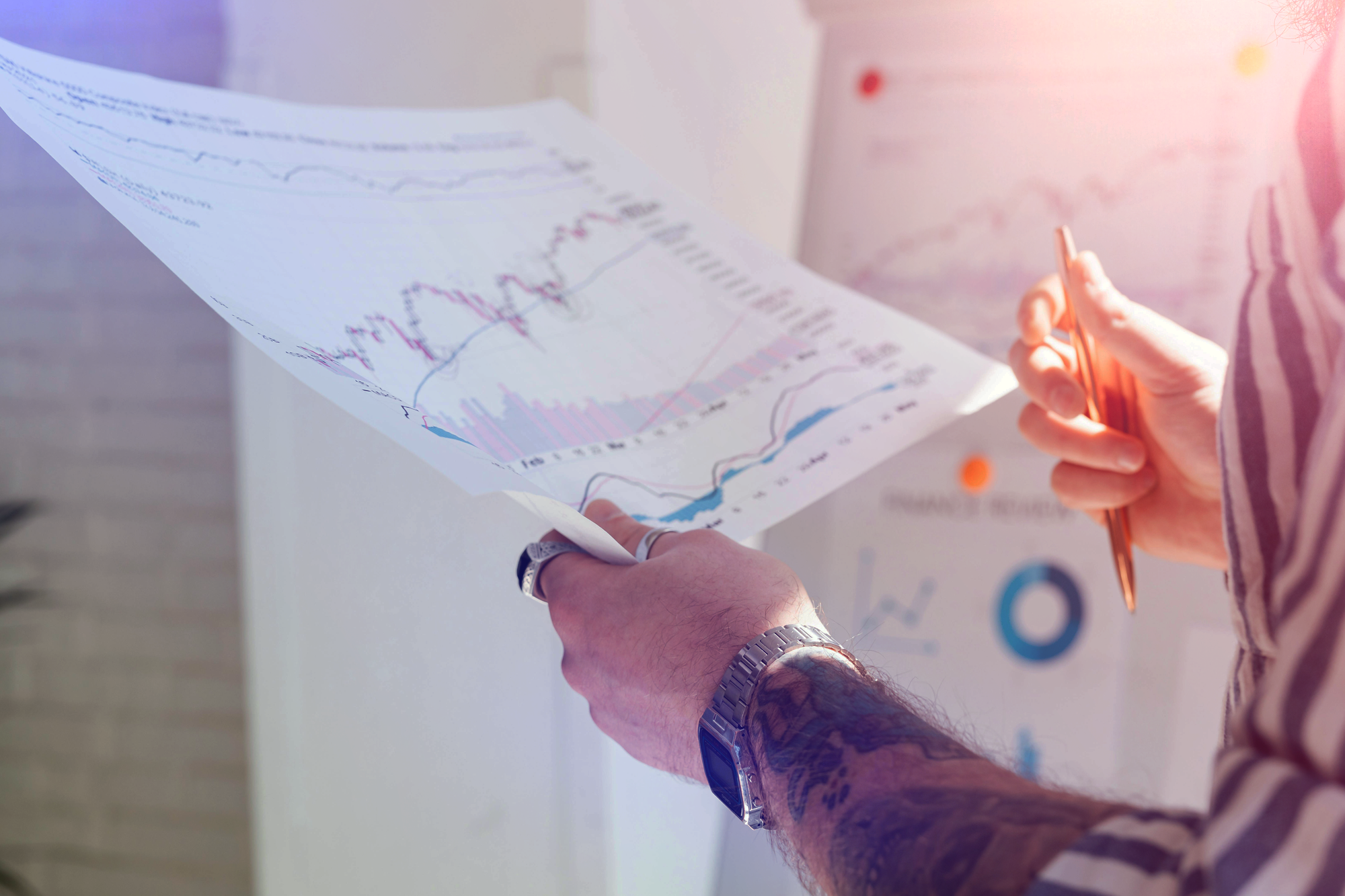 Two people analyze financial charts on printouts during a meeting or presentation.