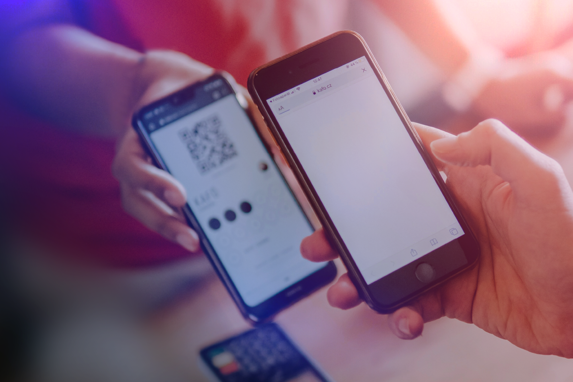 Two people holding smartphones. One person holds a phone displaying a QR code, and the other person holds a phone with an empty screen. A credit card is visible below the phones.